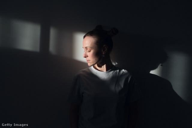 nő a homályban, arca előtt fénysugárral
