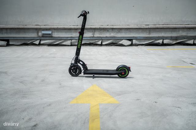 egy elektromos roller áll egy nyíl alakuú, sárga felfestés előtt a betonon