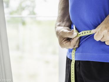 Férfi mérőszalaggal méri fogyásának mértékét.