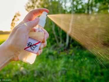 szúnyogriasztót spriccel egy kéz a kertben