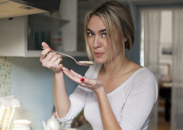 Nő főzés közben a konyhában kóstolja az ételt.