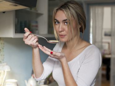 Nő főzés közben a konyhában kóstolja az ételt.