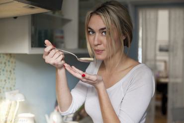 Nő főzés közben a konyhában kóstolja az ételt.