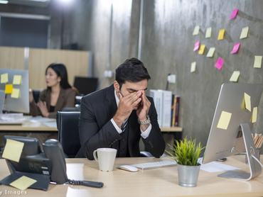 férfi az irodában az asztalnál ül, dörzsöli a szemét, fáradt.