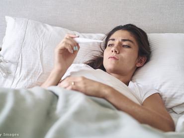 egy beteg nő fekszik a kórházi ágyon, a lázmérőt nézi