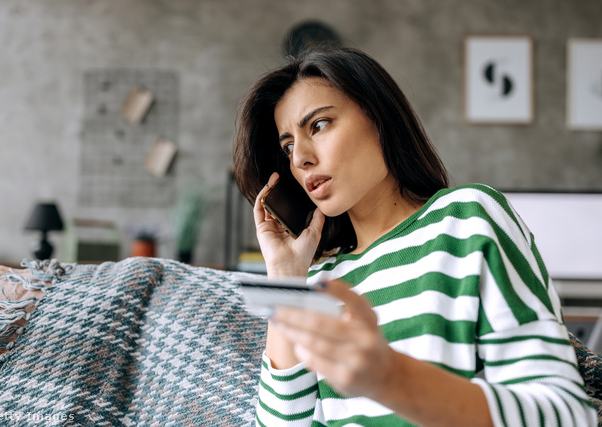 kétségbeesett nő telefonál, másik kezében bankkártyát tart, miközben a kanapén ül