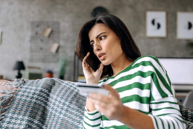 kétségbeesett nő telefonál, másik kezében bankkártyát tart, miközben a kanapén ül