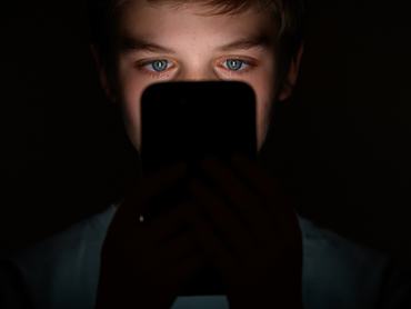 gyerek a sötétben, arcát a mobiltelefon világítja meg