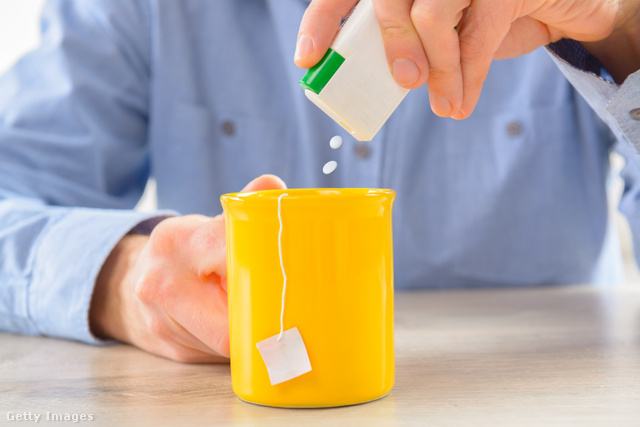 Férfi kék ingben édesítőtablettát tesz egy bögrényi teába.