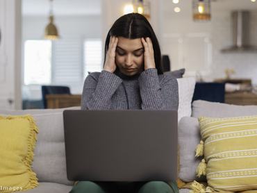 Fiatal nő a fejét fogva ül a laptop előtt a kanapén