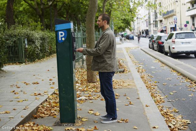 Férfi a parkolóautomatánál vesz jegyet az őszi utcán