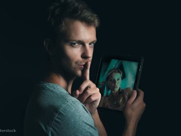 Egy férfi egyik kezében tablettel, a másikkal csendet mutat