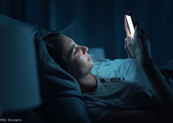Egy nő sötétben, az ágyban fekve nézi a világító telefonját
