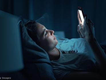 Egy nő sötétben, az ágyban fekve nézi a világító telefonját