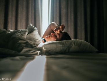 Nő a kezét a fejére teszi, hanyatt fekszik és aludni próbál, miközben fénysugár világítja meg a fejét