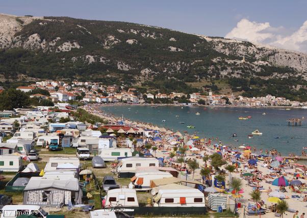 egy nyaralóhely látképe tengerparttal és lakókocsikkal a nyári napsütésben, a strandon sok napernyő