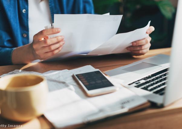 laptop előtt számol egy ember, az asztalon dokumentumok és számológép