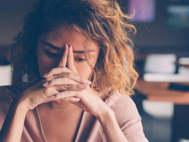 Closeup of sad young Asian woman at cafe leaning head on clasped hands and staring into vacancy. Tired freelancer feeling burnout. Stress and bad news concept