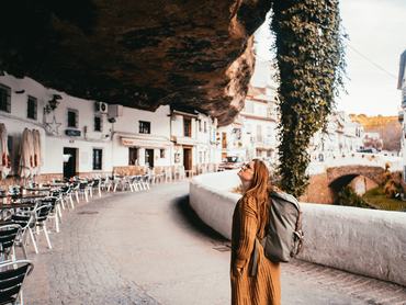 Young female tourist with a backpack is locking above in a small spain village that is build into a rock.