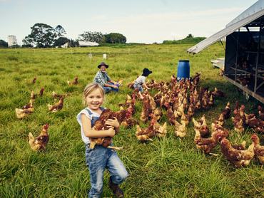 Shot of a little girl holding a chicken while with her family on a farm
