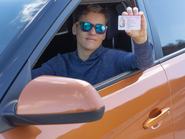 Happy teenager is showing his driving license from open car window. Driving school concept