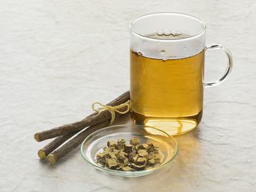 Egy pohár édesgyökér tea és gyökérdarabkák a csésze előtt.
