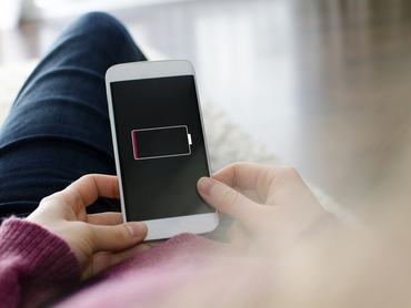 Egy nő mobiltelefont tart a kezében. Az okostelefon készülék képernyőjén egy üres akkumulátor látható.
