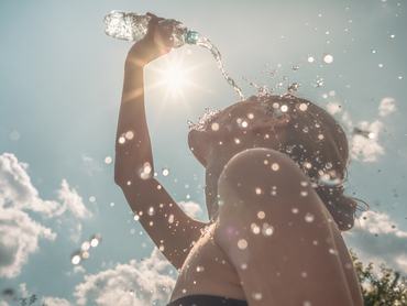 Egy nő egy forró, napsütéses napon egy palack vízzel locsolja magát, hogy lehűtse magát.
