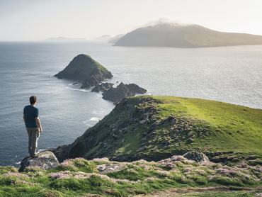 Republic of Ireland, Munster province, County Kerry: high angle view of man gazing at the promontory of Dunmore Head in summer, with Blasket islands in the background.