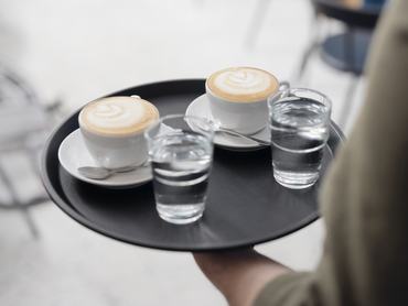 Két coffee latte mellé vizet szolgál fel egy pincér a tálcán