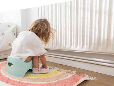 Rear side view of unrecongnizable toddler girl sitting on a potty. Concept of home life.