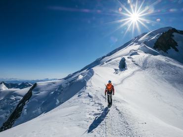 Before Mont Blanc (Monte Bianco) summit 4808m last ascending. Team roping up Man with climbing axe dressed high altitude mountaineering clothes with backpack walking by snowy slopes with blue sky.