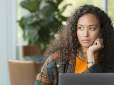 Gondolkodó nő kifele néz az ablakon a laptop előtt ülve