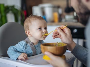 Egy apa otthon eteti kanállal kisfiát.