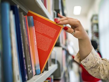 Woman's hand picking a book from a library bookshelf