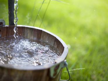 Fresh water from a well flows out into an old bucket. Shallow depth of field for focus on water.