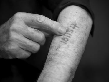 egy férfi mutatja a karján a rá tetovált számot