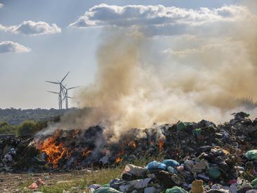 Nagy füsttel égő szeméthalom, háttérben szélerőművekkel