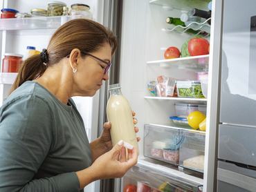 Disgusted woman smelling expired milk by the fridge