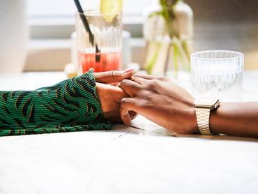 Két ember níugtatóan fogja egymás kezét egy asztalnál ülve