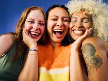 Three Gen Z women laughing together on blue background