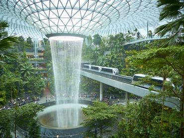 Singapore- Dec, 12, 2024: Futuristic indoor waterfall surrounded by lush vegetation with a skytrain passing by at jewel changi airport, singapore