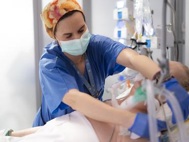 Sebészeti maszkot és kesztyűt viselő ápoló, aki az intenzív osztályon egy intubált beteg lélegeztetőgépét állítja be