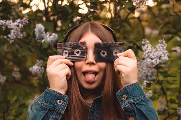 Happy young woman holding audio cassettes in front of her eyes while listening music in headphones during spring