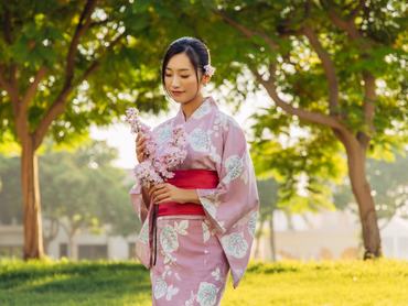 Egy nőtradícionális rózsaszín kimonóban van, kezében egy cseresznyevirággal.