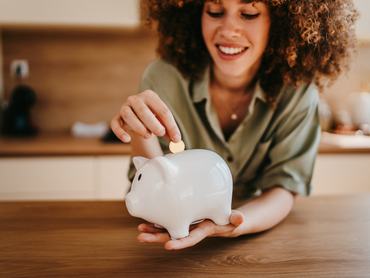 Young woman putting a coin in a piggy bank, managing personal finances and saving for the future