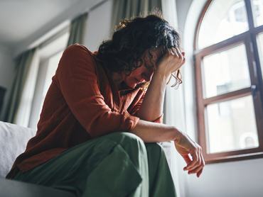 Egy nő karjára támaszkodva gondterhelten ül a kanapén