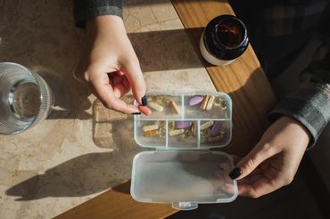 Női kéz kapszulákat rendez egy vitamintartóban