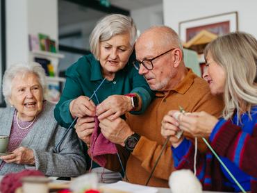 Group of senior people learning knitting together with a caregiver tutor in a community center.