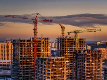 Multiple unfinished apartment buildings with visible concrete frames and tower cranes in a dense urban area during evening light. Image is suitable for illustrating residential development, construction industry, or urban growth.